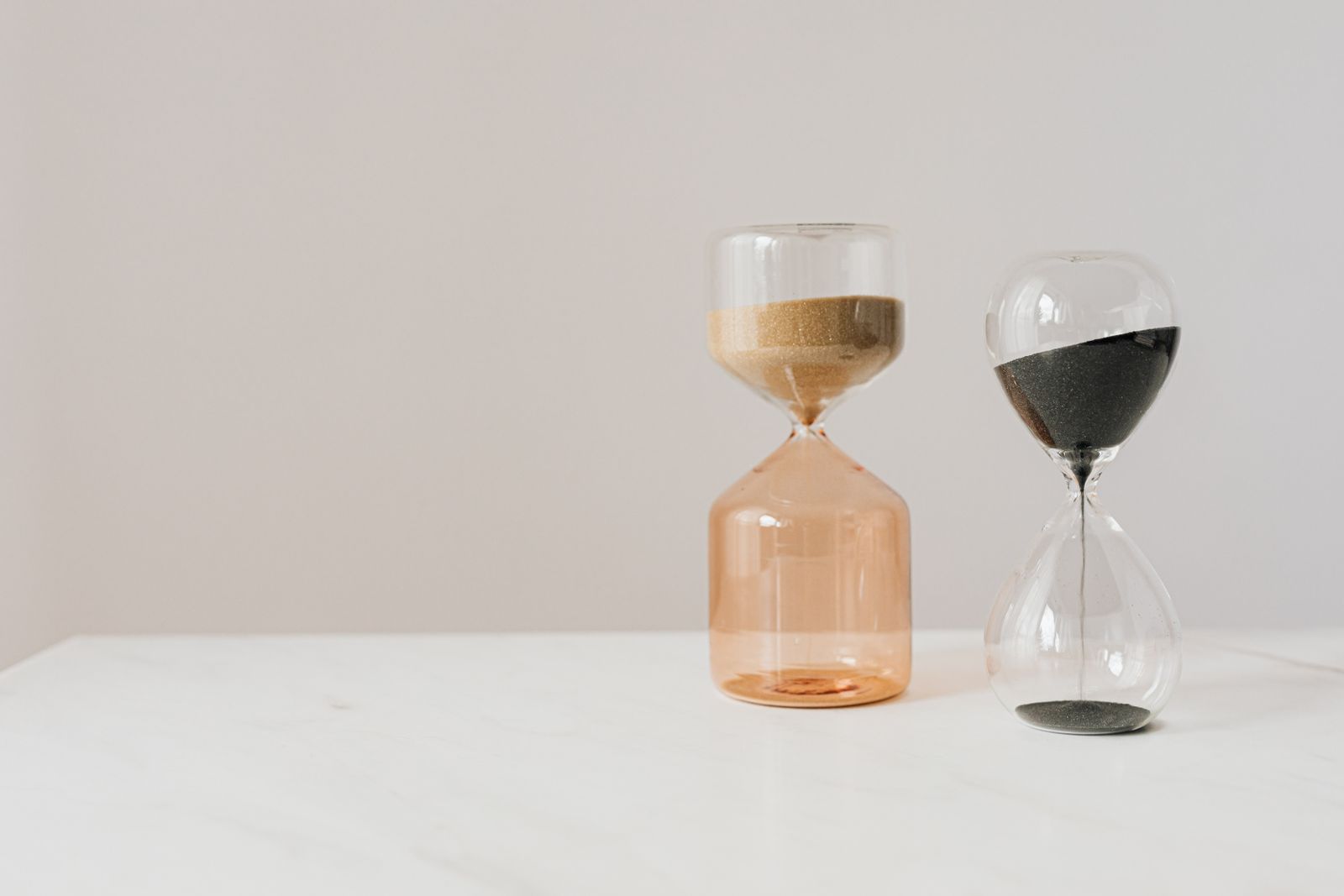 Two hourglasses side by side, one darker and one lighter, both mid-run