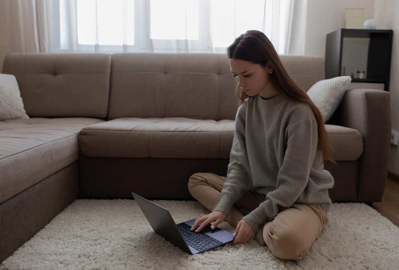 A smiling woman working on a laptop at home in a bright, cozy space